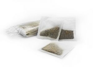 Flat tea bags filled with loose leaf tea, displayed in a stack, made by Custom Co-Pak, a private label tea packaging company in the USA, on a white background.