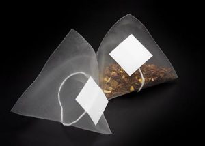 Two transparent pyramid tea bags filled with loose leaf tea, made by Custom Co-Pak, a private label tea packaging company in the USA, displayed on a black background.